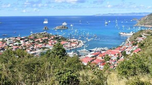 A coastal town with red-roofed buildings, a marina with boats, and a clear blue sky.