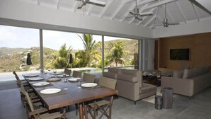Un comedor moderno con una mesa larga dispuesta para una comida, un sofá y un televisor en la pared.