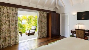 Une chambre d’hôtel avec un lit, une télévision, un bureau avec une chaise et une vue sur les palmiers par la porte ouverte.