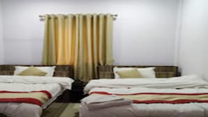 Una habitación con dos camas, cada una con ropa blanca y detalles rojos. Hay una ventana con cortinas, y las paredes son blancas.