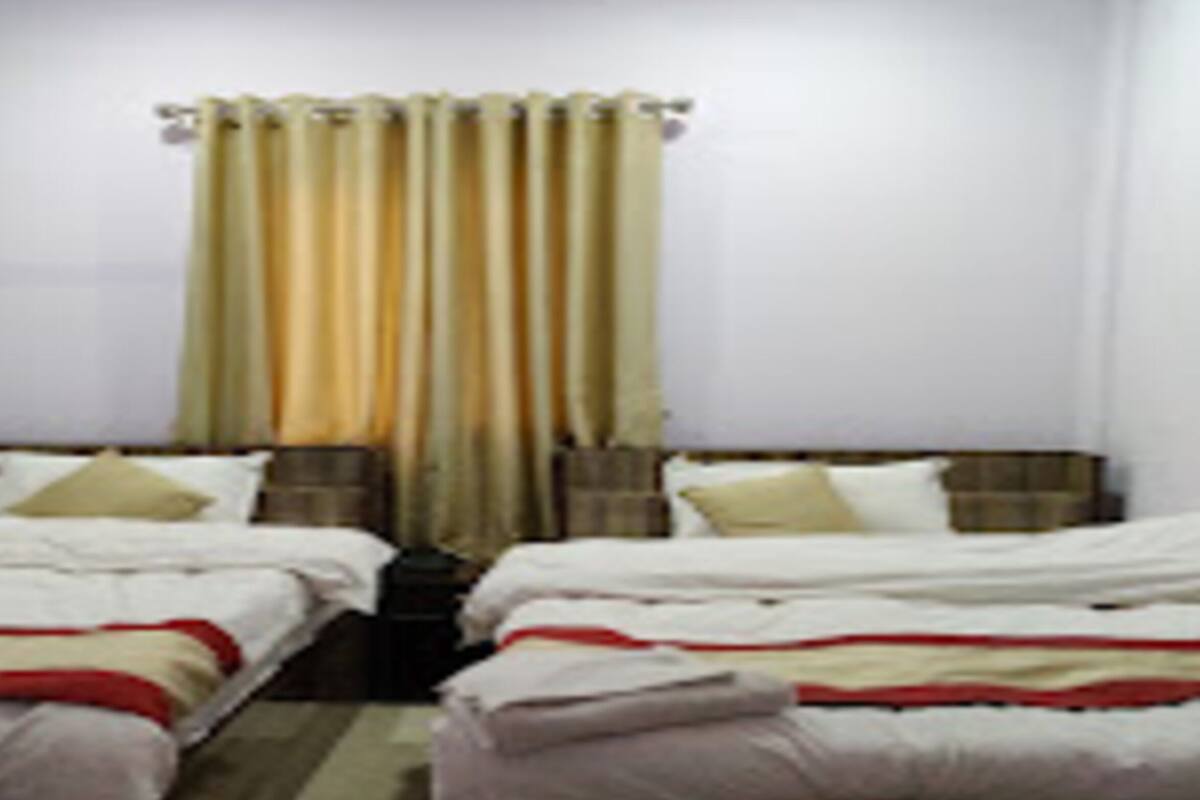 Una habitación con dos camas, cada una con ropa blanca y detalles rojos. Hay una ventana con cortinas, y las paredes son blancas.