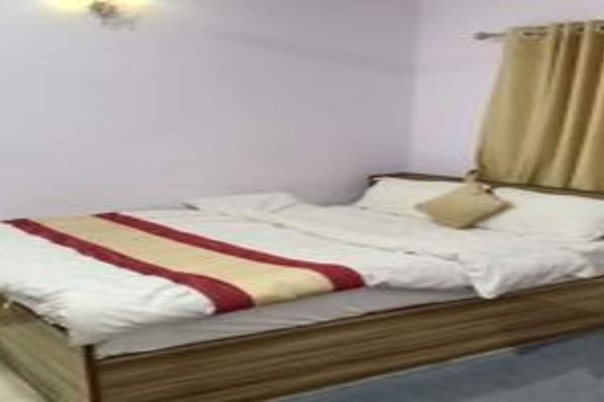 Una cama individual con estructura de madera, ropa de cama blanca y una manta a rayas beige y roja.