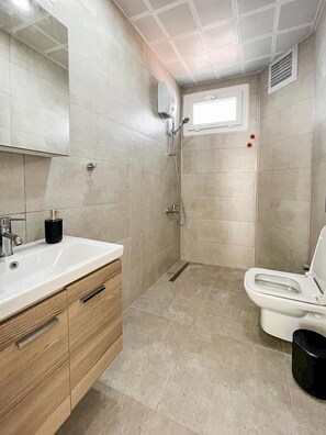 A bathroom with a white sink, wooden cabinet, shower, and toilet. - Green Hill  (Kas)