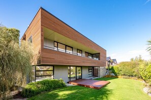 Une maison moderne à deux étages, dotée d’un toit plat, de grandes fenêtres et d’une pelouse bien entretenue.