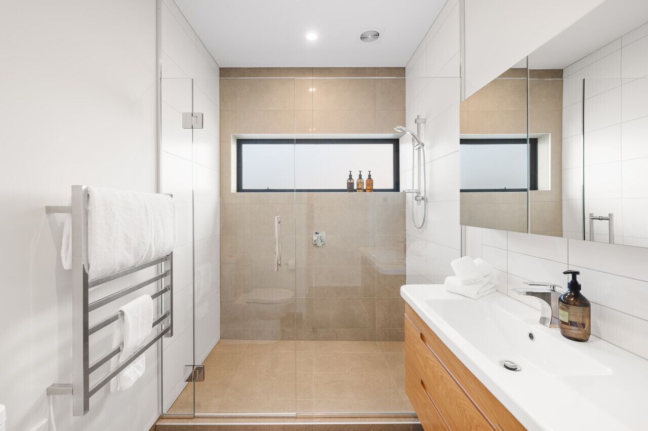 A modern bathroom with a glass-enclosed shower, a large mirror, and a white vanity with a sink and toiletries.