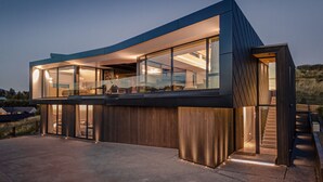 Una casa moderna de dos pisos con amplios ventanales de vidrio, fachada de madera y una escalera visible que conduce al nivel superior.