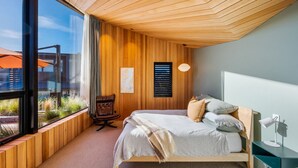 A modern bedroom with a large window, wooden panel walls, a bed with pillows, a desk with a lamp, and a chair. - Hideaway on Warren Wanaka (Wanaka)
