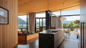 A modern kitchen with a large island, wooden ceiling, and large windows offering a view of mountains. - Hideaway on Warren Wanaka (Wanaka)