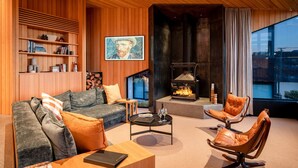 A modern living room with a fireplace, wooden paneling, a sofa, a coffee table, and a bookshelf. - Hideaway on Warren Wanaka (Wanaka)