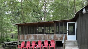 Eine rustikale Holzhütte mit überdachter Veranda, Sitzbereich, Picknicktisch und einer Holzterrasse, die zum Eingang führt.