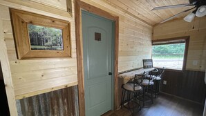Ein Holzinterieur mit einer Tür, einem gerahmten Bild, einer Bar mit Hockern und einem Fenster mit Aussicht.