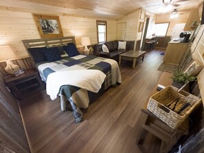 Un accogliente interno di una baita con un letto, un divano, un'area pranzo e una cucina.