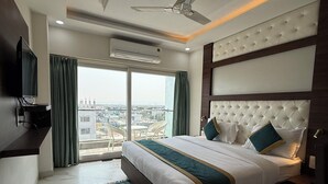 Une chambre d’hôtel moderne dotée d’un grand lit, d’un ventilateur de plafond, d’un climatiseur, d’une télévision et offrant une vue sur la ville par la fenêtre.