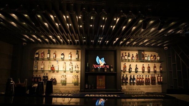 Un bar avec une enseigne au néon, des étagères remplies de bouteilles d’alcool et une vitrine réfrigérée.