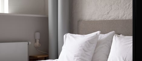 A neatly made bed with white bedding and pillows, a bedside table with a book and glasses, and a wall-mounted phone.