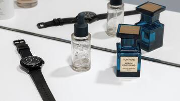 A white surface with various items including a watch, perfume bottles, and a bottle of hand sanitizer.