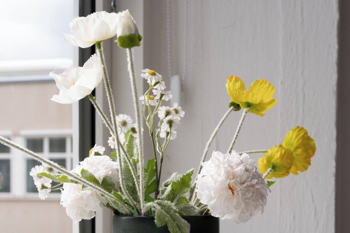 A vase with white and yellow flowers on a windowsill.