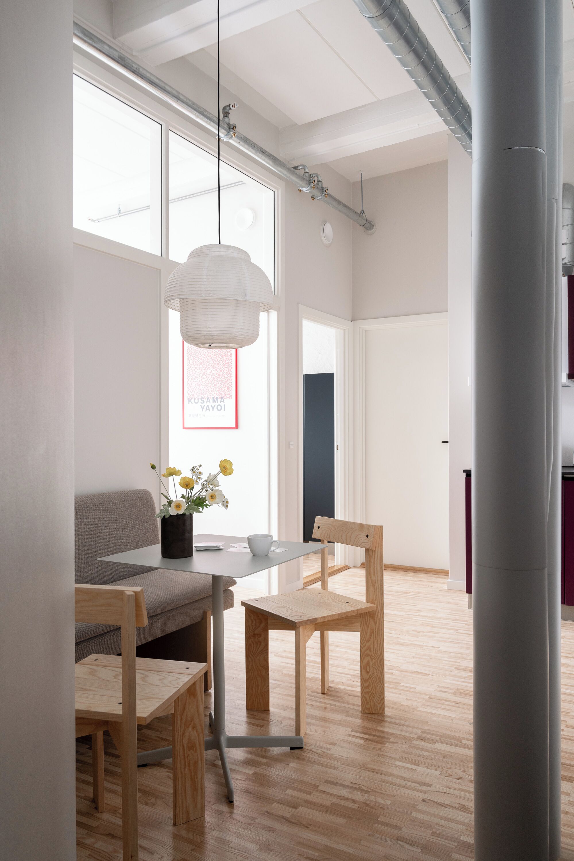 Ein modernes Interieur mit Holzboden, einem Esstisch mit Stühlen, einer Pendelleuchte und einem Fenster mit Aussicht.