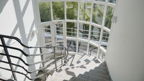 Una escalera con barandilla metálica que lleva a un balcón de paredes de vidrio con vistas a la ciudad.