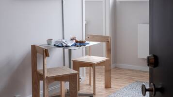 Una habitación con televisión montada en la pared, dos sillas de madera, una mesita con una taza y un libro, una ventana con vistas al exterior y una puerta.