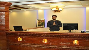 A reception desk with a laptop, a monitor, and a person standing behind it. - MeroStay 218 HK HE (Nagarjun)