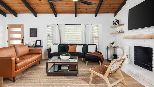 Ein Wohnzimmer mit Ledersofa, Glastisch, Holzboden, Kamin und Wand-Fernseher.