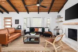 A living room with a leather sofa, a glass coffee table, a wooden ceiling, a fireplace, and a TV mounted on the wall.