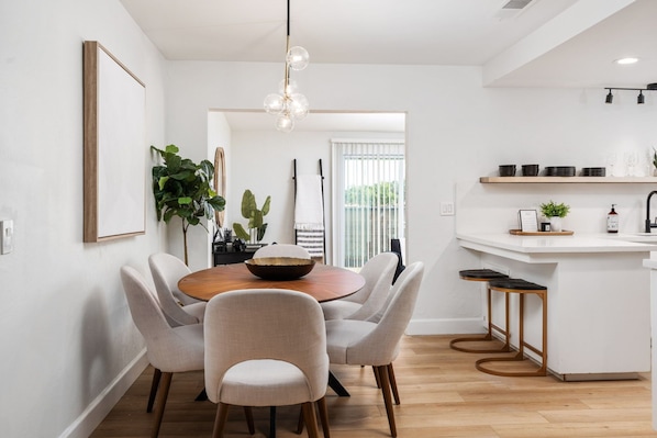 A modern kitchen with a round dining table, light-colored chairs, and a white countertop with bar stools.