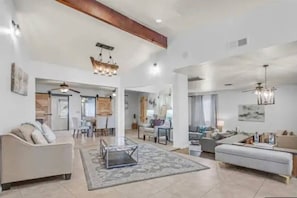 A spacious living area with a sofa, a coffee table, and a chandelier. There is a dining area with chairs and a table.
