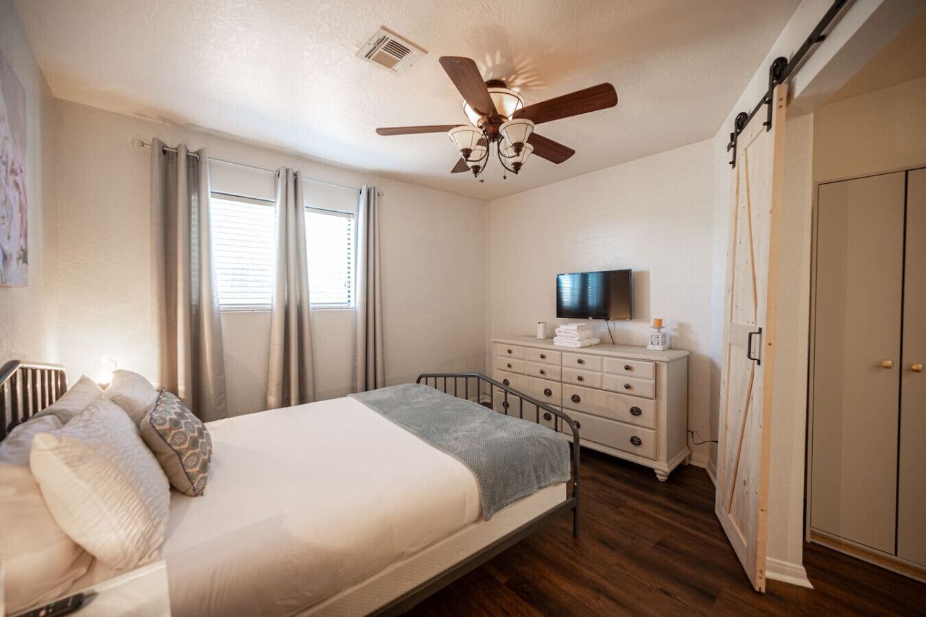 A bedroom with a bed, dresser, TV, and a ceiling fan.