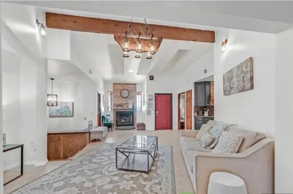 A spacious living room with a fireplace, a sofa, a coffee table, and a kitchen area visible through an open door.