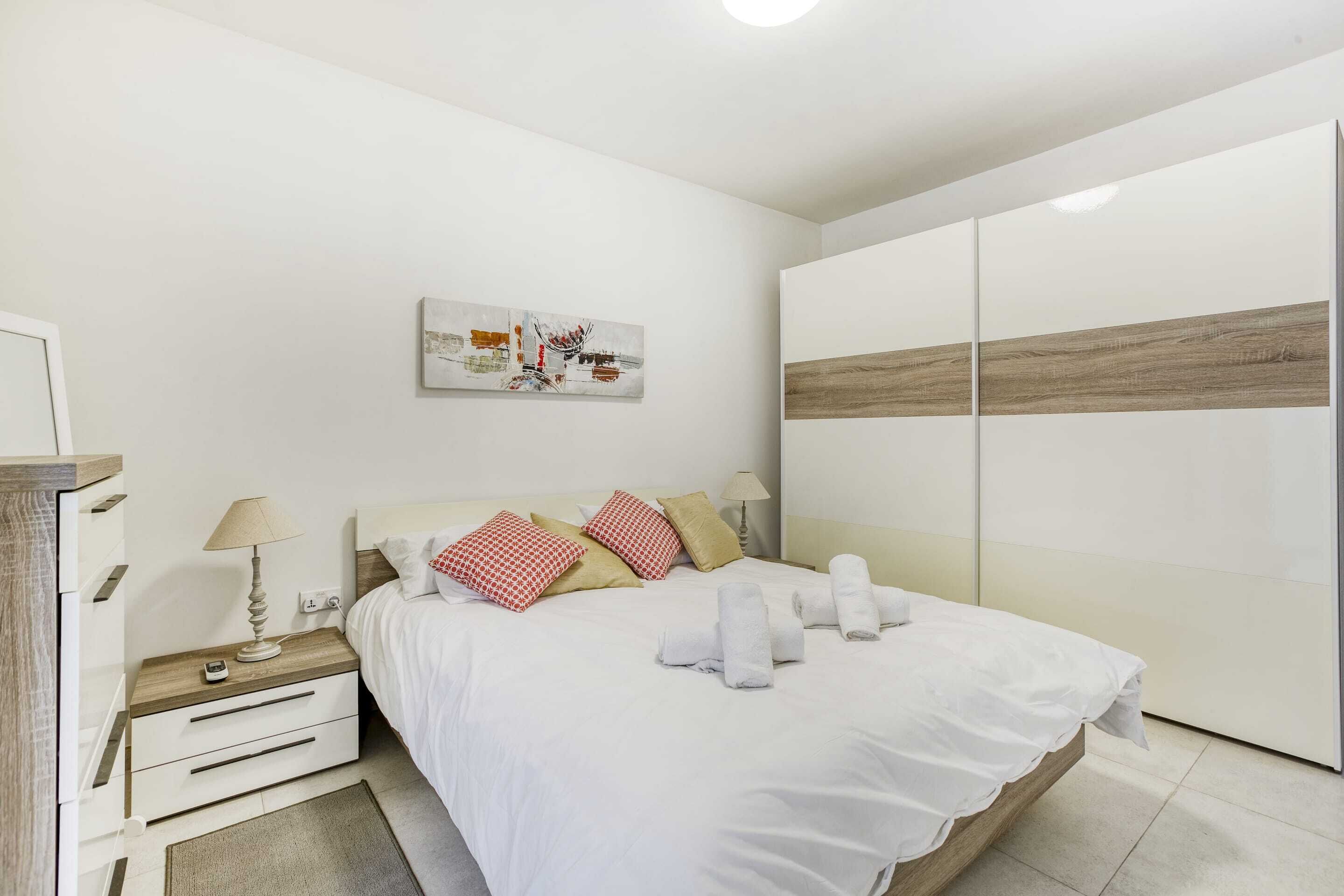 A modern bedroom with a bed, bedside tables, a wardrobe, and a wall art piece.