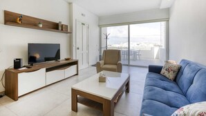 A modern living room with a TV, sofa, coffee table, and a balcony with a view. - Gzira Penthouse (Gzira)