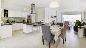A modern kitchen with white cabinets, a central island, and a dining area with a table set for four. - Gzira Penthouse (Gzira)