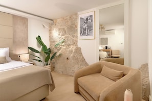 Quarto de hotel moderno com uma cama grande, um sofá, parede decorada com pedra, um quadro emoldurado e uma planta em vaso.