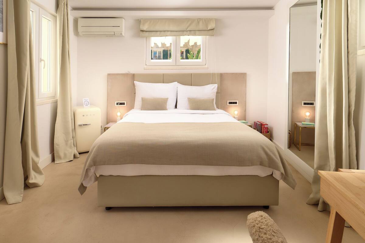 Een slaapkamer met een groot bed, nachtkastjes, een raam met gordijnen en een spiegel.