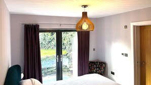 A bedroom with a bed, a hanging light fixture, a chair, and a door.