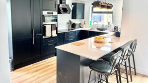 A modern kitchen with dark cabinetry, a central island, bar stools, and a large window providing natural light.