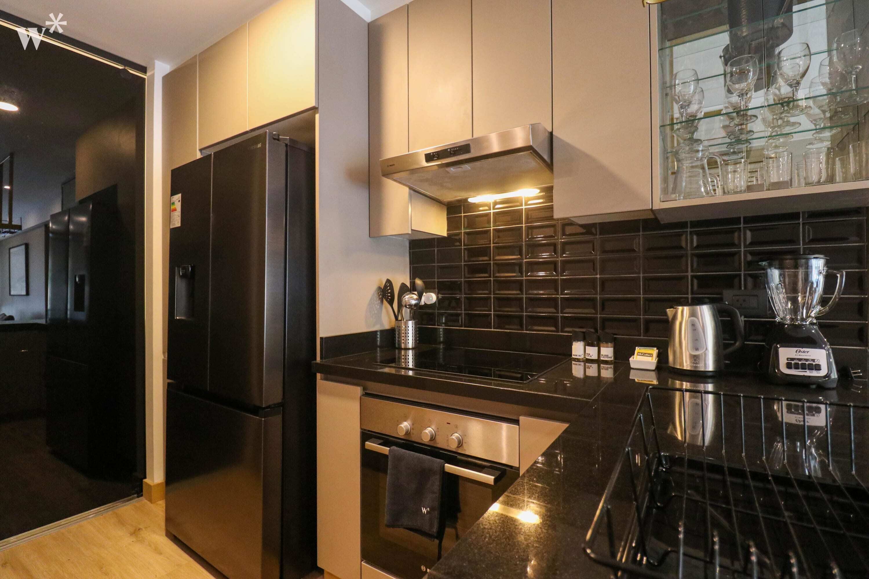 A modern kitchen with stainless steel appliances, a black countertop, and a backsplash.