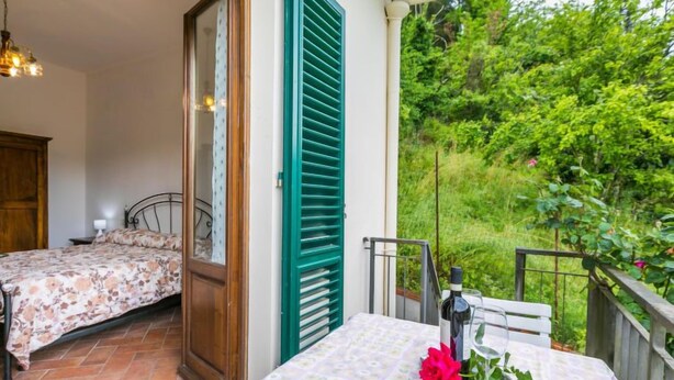 Un dormitorio con cama, mesita de noche y ventana con contraventanas verdes.