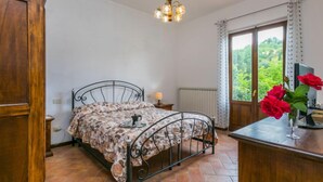 Un dormitorio con una cama, un armario de madera, un escritorio con una computadora, una ventana con cortinas y una araña.
