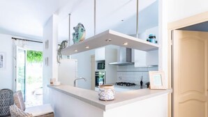 Une cuisine moderne avec des meubles blancs, un îlot central et un coin repas doté de chaises en osier.