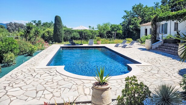 Une piscine rectangulaire bordée de pierres, entourée d’une terrasse agrémentée de chaises longues et de plantes en pot.