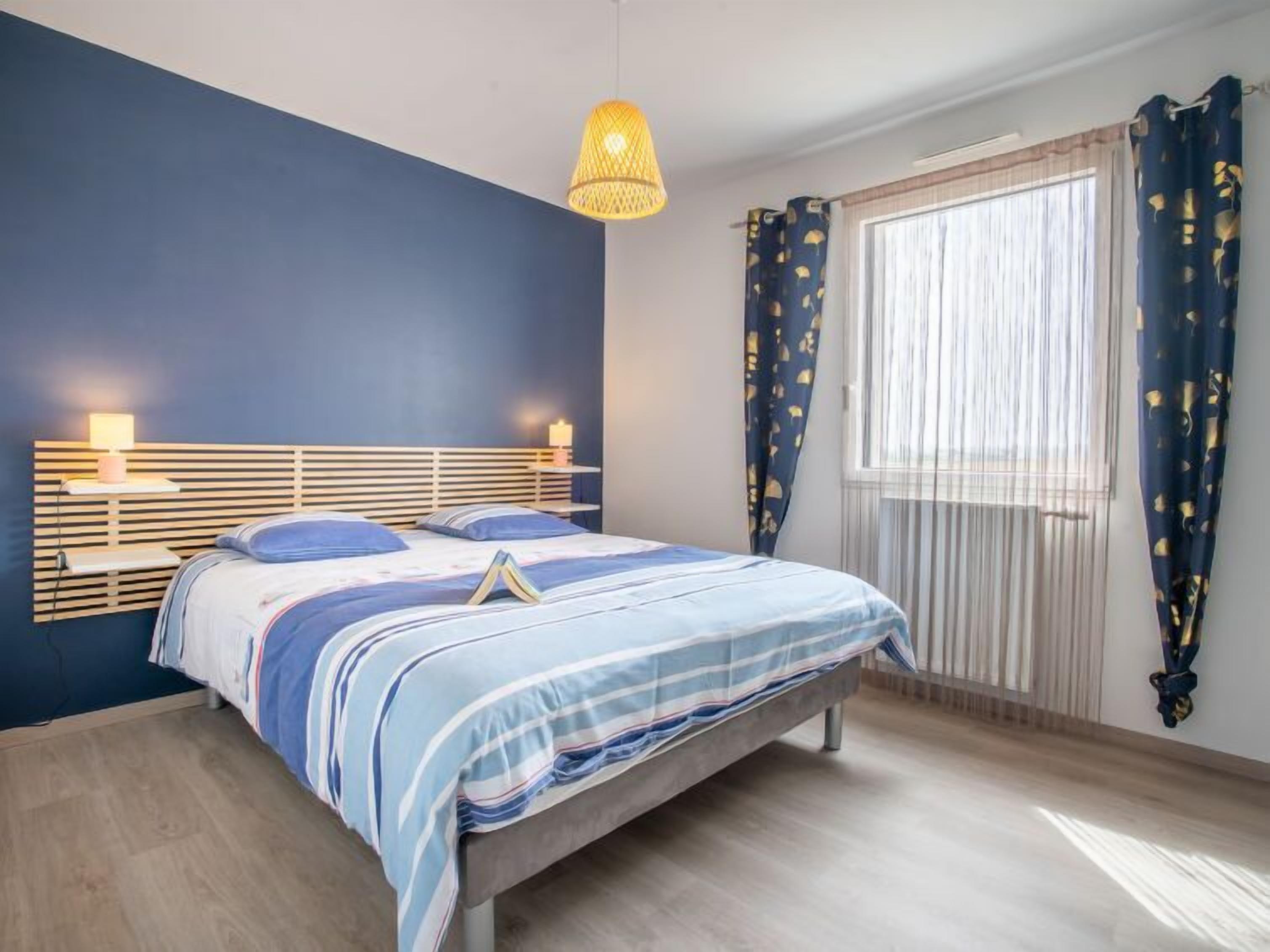Ein Schlafzimmer mit Bett, Nachttischlampen, einem Fenster mit Vorhängen und einer Pendelleuchte.