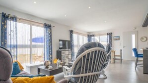 Una sala de estar moderna con un sofá, una silla, un televisor y un comedor con mesa y sillas.