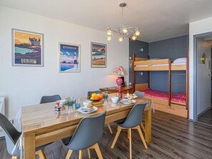 Une pièce de taille modeste comprenant un lit superposé, une table à manger en bois avec des chaises et un lustre.