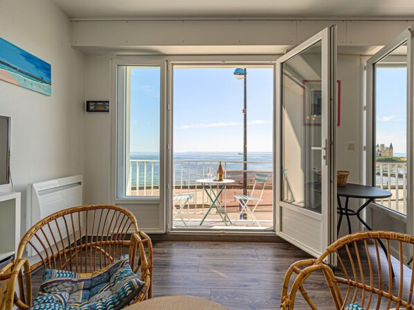 Une pièce avec vue sur la mer, une table avec des chaises et deux fauteuils en osier.