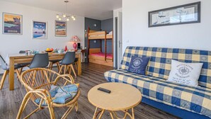 Ein gemütliches Zimmer mit einem Etagenbett, einer Essecke mit Stühlen und einem Tisch sowie einem Sofa mit kariertem Kissen.