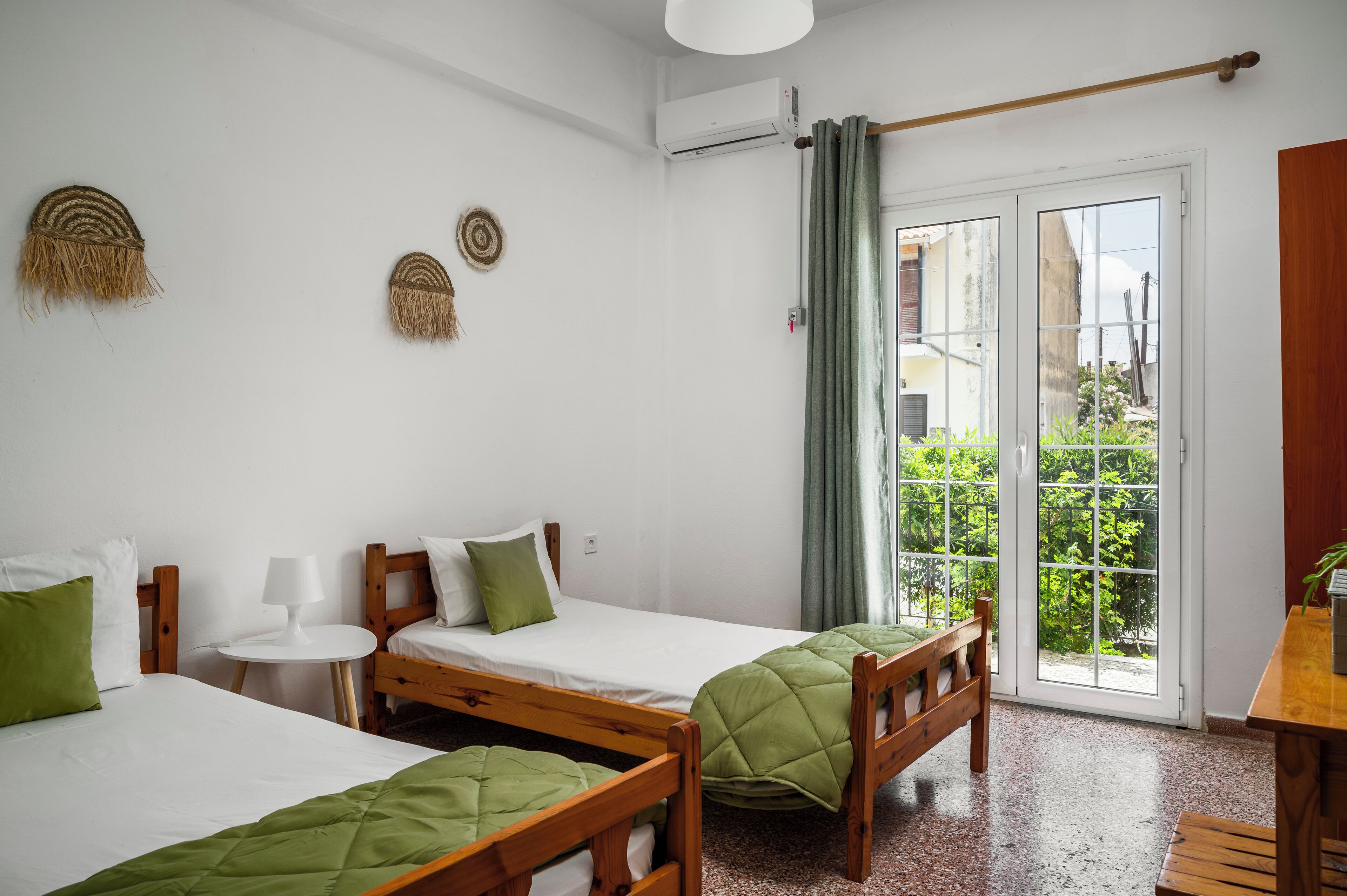A room with two wooden beds, a small round table, and a view of greenery through a sliding door.