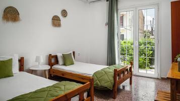 A room with two wooden beds, a small round table, and a view of greenery through a sliding door.